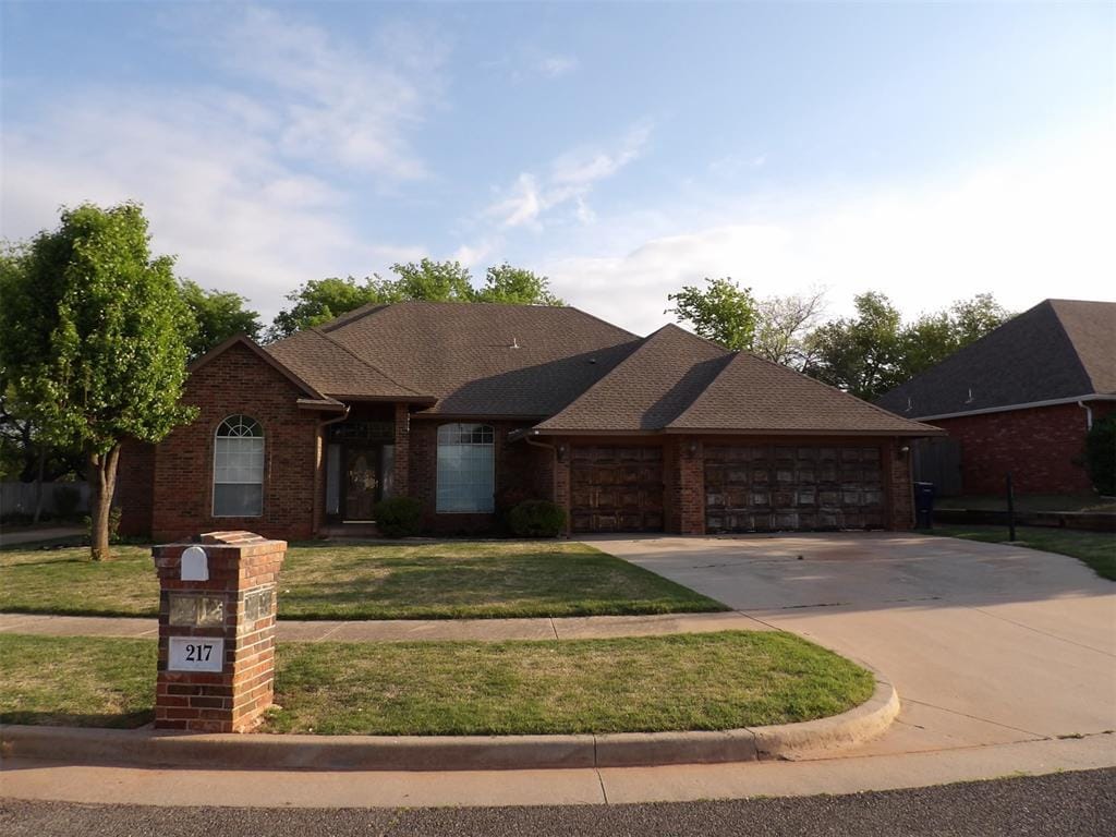 view of front of house featuring a front lawn, roof with shingles, driveway, brick siding, and a garage