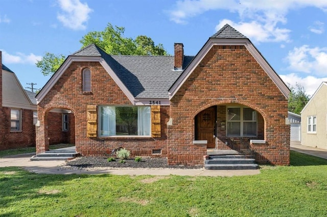 view of front of property featuring a chimney, brick siding, and a front lawn