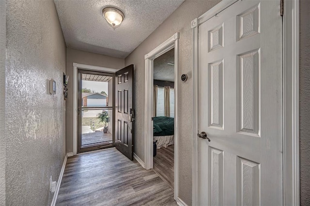 entryway featuring wood finished floors, a textured ceiling, baseboards, and a textured wall