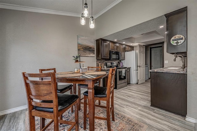 dining room featuring light wood finished floors, ornamental molding, washer / dryer, baseboards, and a textured ceiling