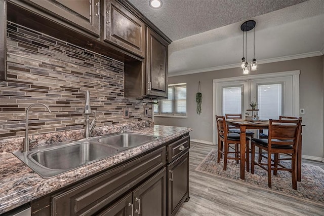 kitchen with dark brown cabinetry, a sink, backsplash, and crown molding