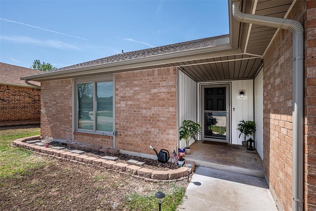 entrance to property with a shingled roof and brick siding