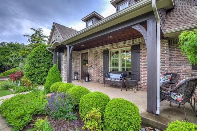 doorway to property featuring covered porch, a shingled roof, and brick siding