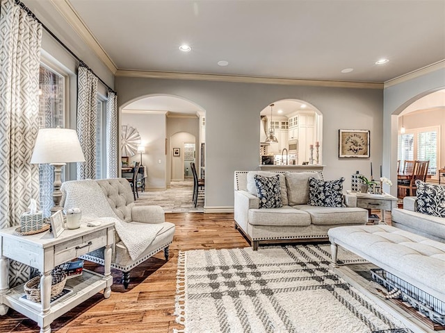 living room with crown molding, arched walkways, baseboards, and wood finished floors