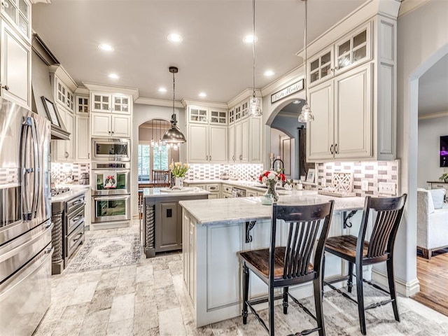 kitchen with stainless steel appliances, arched walkways, ornamental molding, and a center island