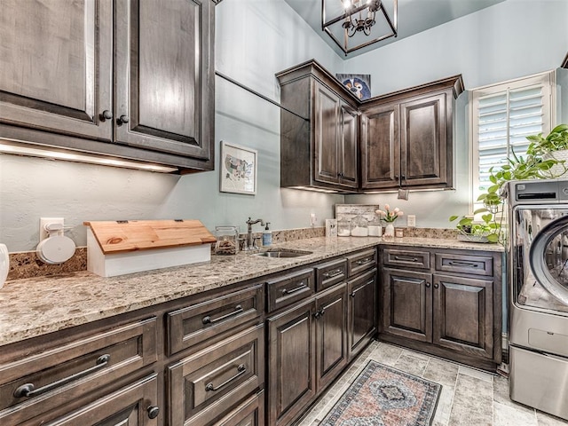 washroom with cabinet space, a notable chandelier, washer / dryer, and a sink