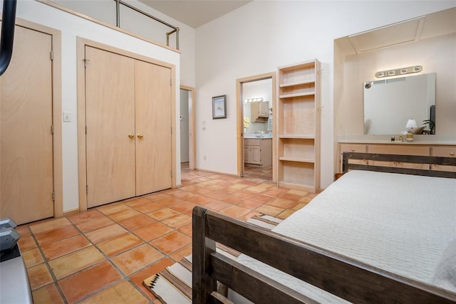 bedroom featuring a closet, a towering ceiling, light tile patterned flooring, baseboards, and ensuite bath