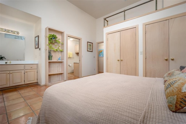 bedroom with connected bathroom, a towering ceiling, two closets, and light tile patterned flooring