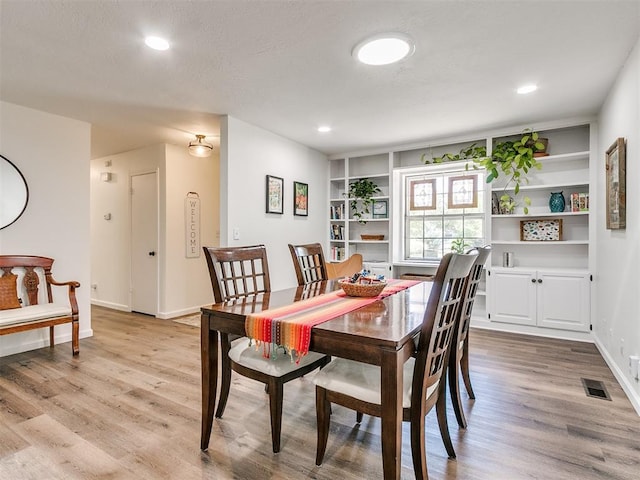 dining space featuring built in features, baseboards, wood finished floors, and visible vents