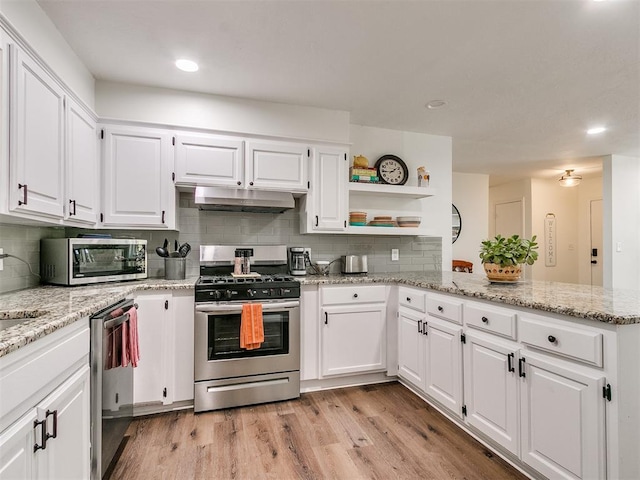 kitchen featuring appliances with stainless steel finishes, tasteful backsplash, a peninsula, under cabinet range hood, and white cabinetry