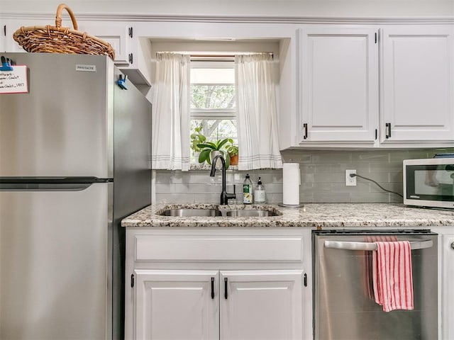 kitchen featuring light stone counters, a sink, stainless steel appliances, white cabinetry, and backsplash