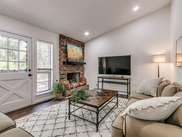 living area with wood finished floors, recessed lighting, a brick fireplace, and lofted ceiling