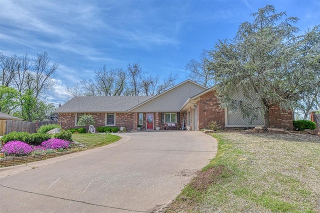 ranch-style house with concrete driveway, brick siding, fence, and a front yard
