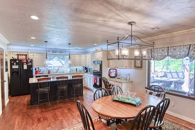 dining space featuring visible vents, crown molding, wood finished floors, a textured ceiling, and a notable chandelier