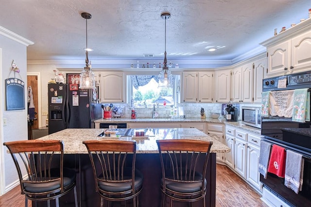 kitchen featuring a sink, tasteful backsplash, a kitchen island, ornamental molding, and black appliances