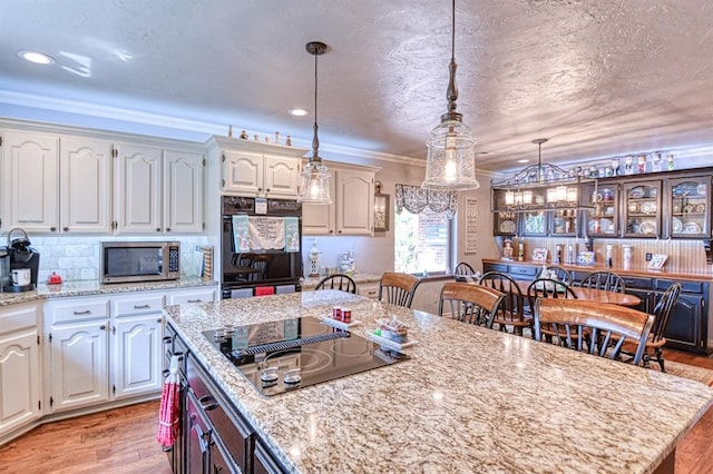 kitchen featuring a kitchen island, decorative light fixtures, black appliances, light wood finished floors, and white cabinetry