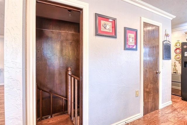 hall with crown molding, baseboards, a textured wall, and wood finished floors