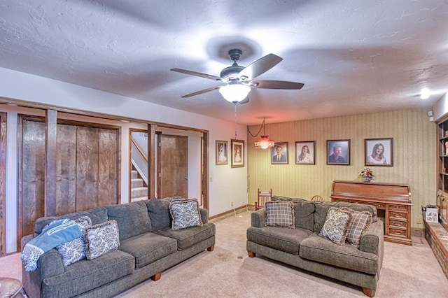living room with light colored carpet, a ceiling fan, stairs, and baseboards