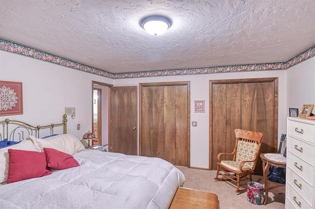 bedroom with two closets, a textured ceiling, and carpet