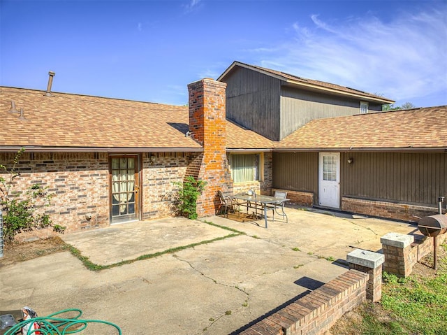 back of property featuring a shingled roof, brick siding, and a patio