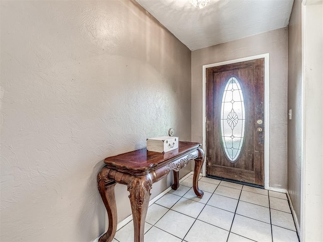 foyer entrance featuring a textured wall, baseboards, and light tile patterned floors