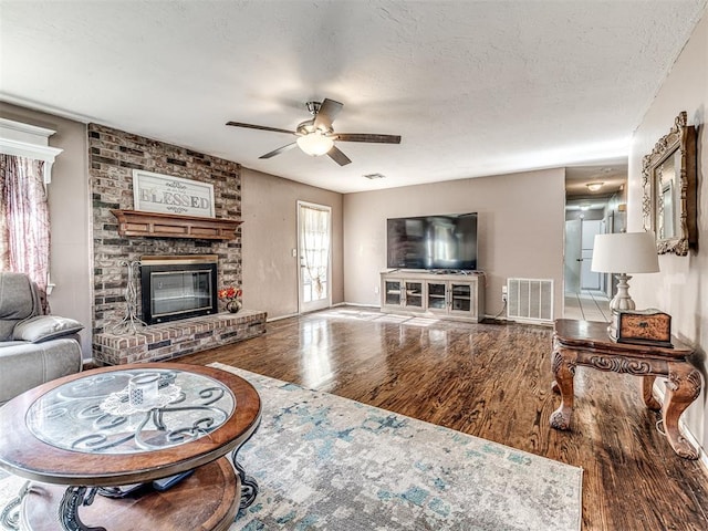 living area with wood finished floors, visible vents, a fireplace, a textured ceiling, and ceiling fan
