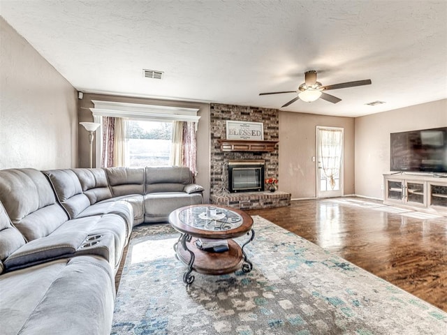 living area with wood finished floors, a brick fireplace, a ceiling fan, and a wealth of natural light