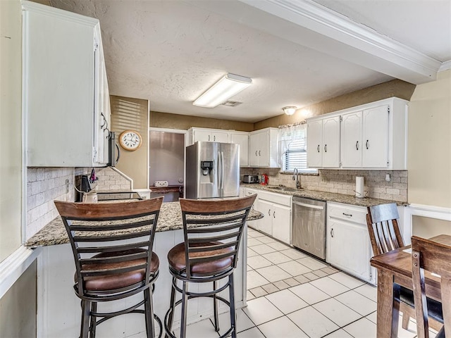 kitchen featuring stainless steel appliances, a sink, decorative backsplash, a peninsula, and white cabinetry