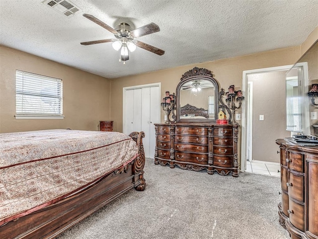 carpeted bedroom with visible vents, a textured ceiling, a closet, and ceiling fan