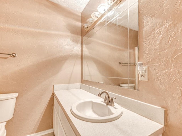 bathroom featuring a textured wall, baseboards, vanity, and toilet