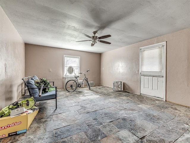 interior space featuring stone tile flooring, a textured wall, a textured ceiling, and ceiling fan