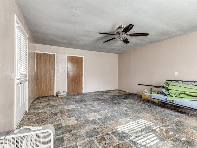 unfurnished bedroom featuring a ceiling fan and stone tile floors