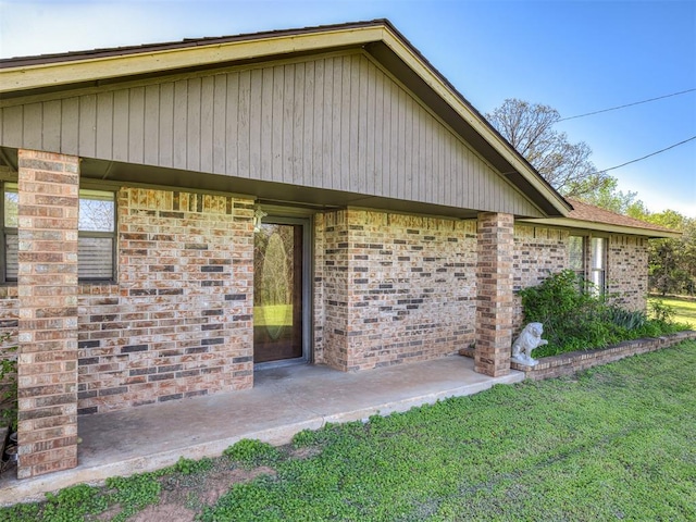 view of side of home with brick siding, a lawn, and a patio
