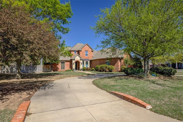 view of front facade with brick siding, a front lawn, fence, and curved driveway