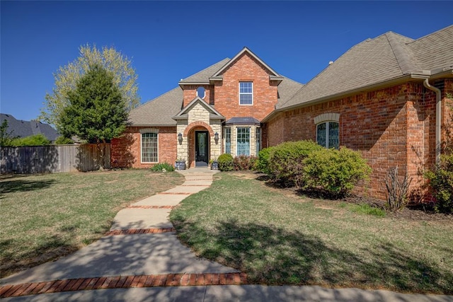traditional-style home featuring brick siding, fence, a shingled roof, and a front yard
