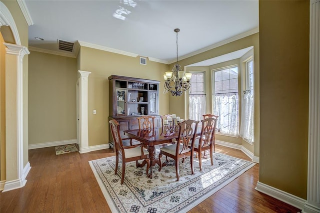 dining room featuring dark wood finished floors, visible vents, baseboards, decorative columns, and a chandelier