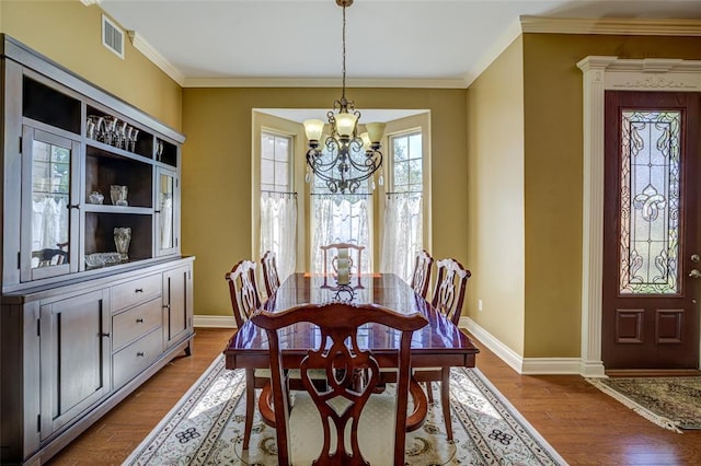 dining area with crown molding, wood finished floors, an inviting chandelier, baseboards, and visible vents