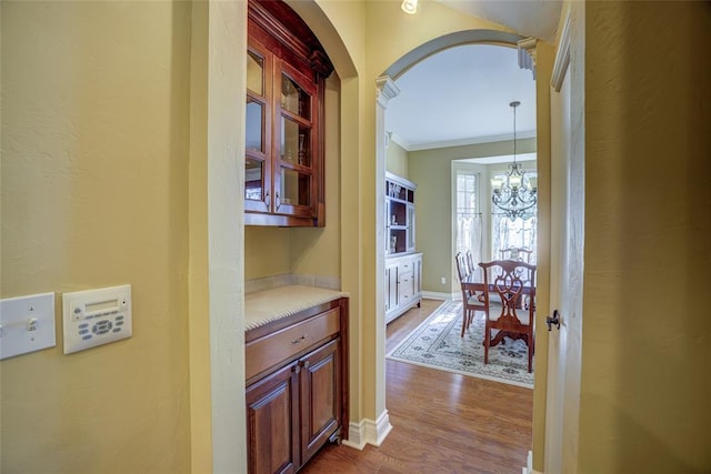 corridor featuring an inviting chandelier, arched walkways, crown molding, baseboards, and dark wood-style flooring