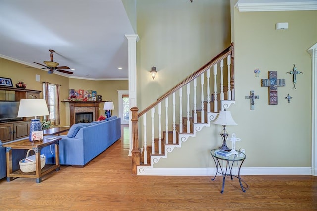 stairway featuring ceiling fan, crown molding, wood finished floors, and a fireplace
