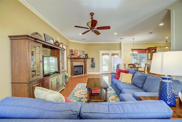 living room with crown molding, ceiling fan with notable chandelier, light wood-type flooring, a tile fireplace, and baseboards
