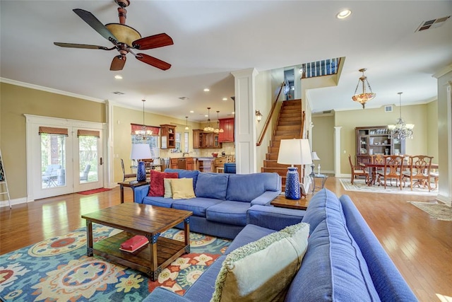 living area featuring stairs, ceiling fan with notable chandelier, light wood-type flooring, baseboards, and ornamental molding