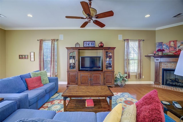 living area featuring baseboards, visible vents, wood finished floors, a brick fireplace, and ornamental molding