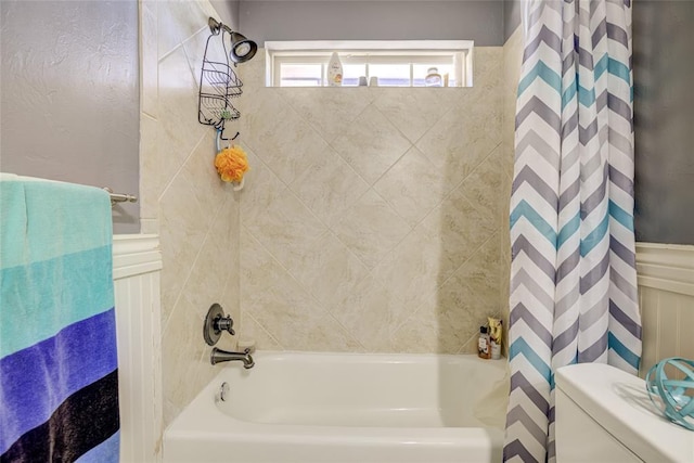 bathroom featuring wainscoting, shower / bath combo with shower curtain, and toilet