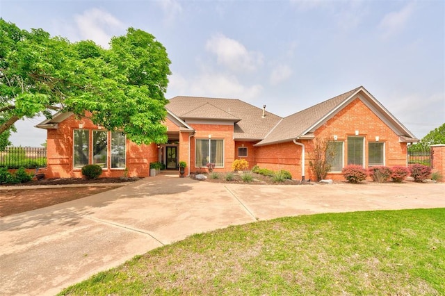 ranch-style home with fence, a shingled roof, a front yard, and brick siding