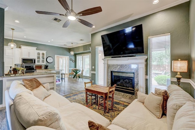 living room featuring crown molding, ceiling fan, wood finished floors, and a healthy amount of sunlight