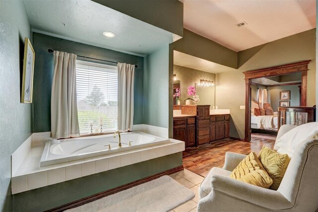 bathroom with connected bathroom, a textured wall, vanity, visible vents, and a garden tub
