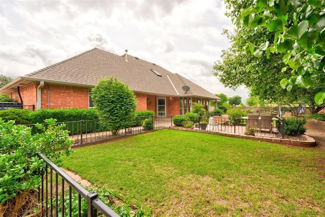 back of house with roof with shingles, fence, a lawn, and brick siding