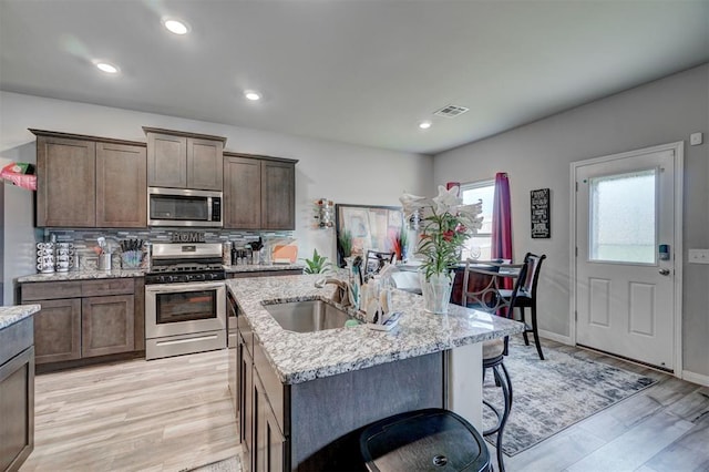 kitchen featuring backsplash, visible vents, light stone countertops, light wood-style floors, and stainless steel appliances
