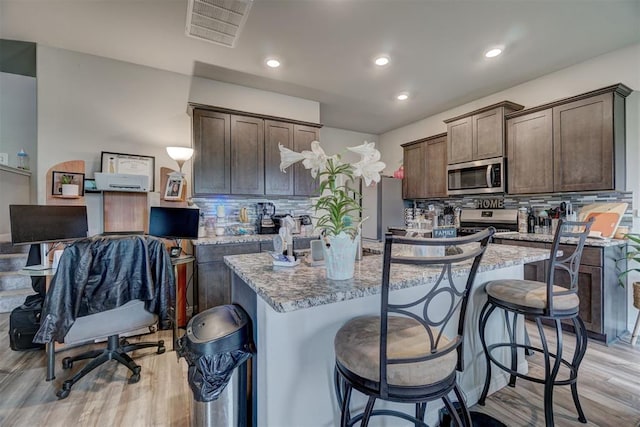 kitchen with dark brown cabinetry, light wood-style floors, stainless steel appliances, backsplash, and visible vents
