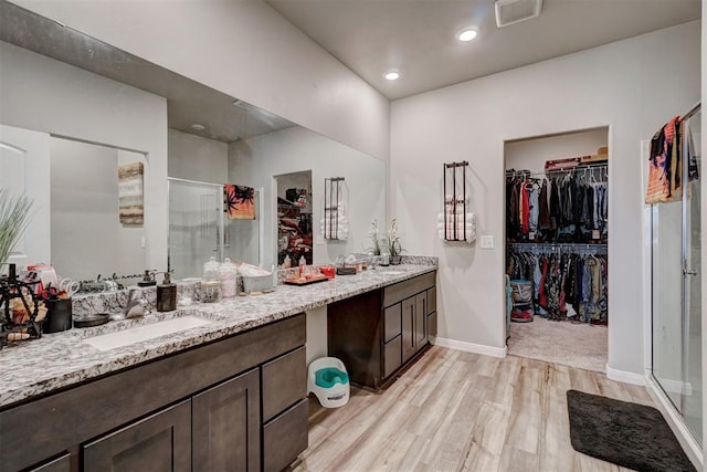 full bathroom featuring a walk in closet, visible vents, a stall shower, wood finished floors, and vanity